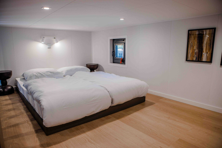 Dormitorio moderno en una cabaña con cama doble, ropa de cama blanca, piso de madera y decoración minimalista.