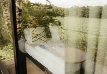 Vista a través de la ventana de Nokken NKN-18 Cabin en Wilsumer Berge, Alemania, rodeada de naturaleza.