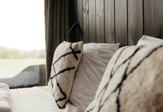 Close-up of a cozy bed with plush pillows and wood panel wall in Nokken NKN-18 Cabin at Wilsumer Berge, Germany.