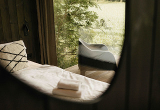 Interior view of Nokken NKN-18 Cabin at Wilsumer Berge in Germany, featuring a bed with outdoor scenery.