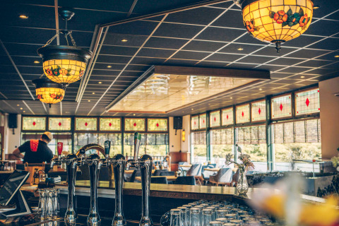 Cozy bar interior with stained-glass lamps and large windows at a glamping accommodation in nature.
