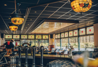 Interno di un bar accogliente con lampade colorate e grandi finestre in una struttura di glamping.