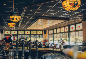 Interiør af en hyggelig bar med farverige glaslamper og store vinduer på et glamping-sted i naturen.