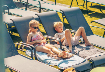 Twee kinderen ontspannen op ligstoelen met handdoeken op een zonnige dag bij een glampingaccommodatie.