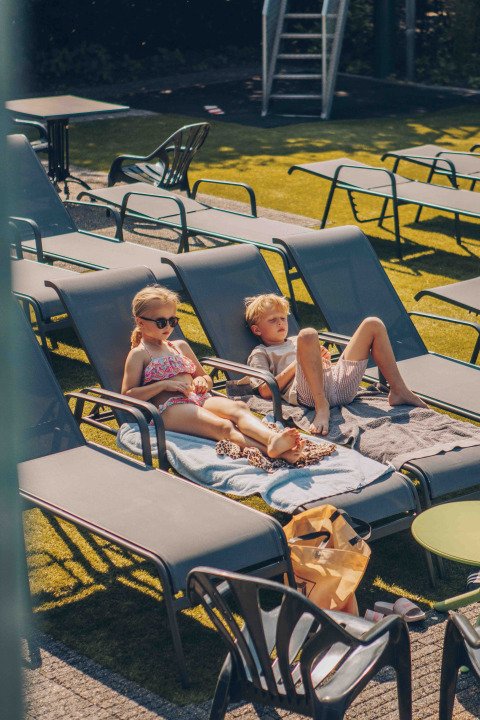 Twee kinderen ontspannen op ligstoelen met handdoeken op een zonnige dag bij een glampingaccommodatie.
