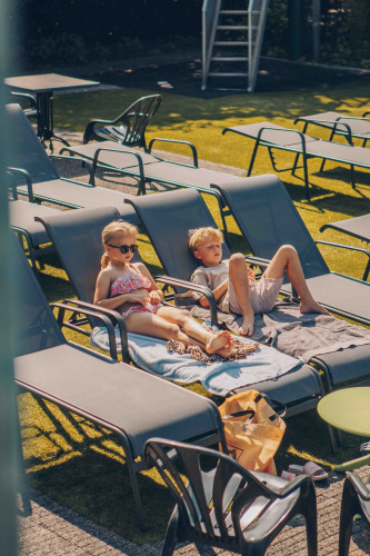 Two children relaxing on sun loungers with towels on a sunny day at a glamping accommodation outdoors.