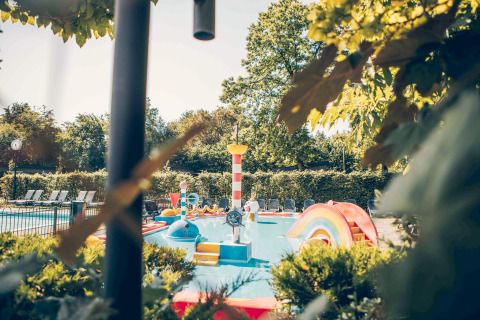 Colorful kids’ splash pool and playground at a glamping accommodation, surrounded by greenery.