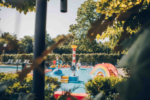 Bunter Kinderspielplatz mit Pool und Rutsche in einer Glamping-Unterkunft umgeben von Bäumen.