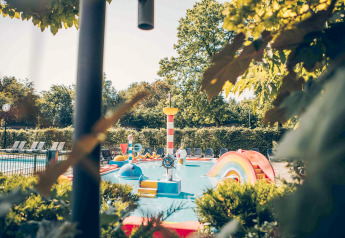 Kleurrijk kinderbadje en speeltuin op een glamping locatie omringd door groene struiken en bomen.