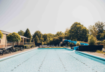 Outdoor swimming pool with waterslide and sun loungers at a glamping accommodation on a sunny day.
