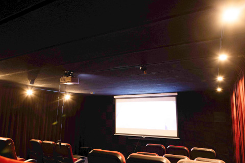 Salle de cinéma sombre avec sièges rouges vides, écran lumineux et éclairage doux dans un glamping.