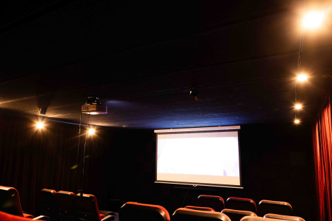 Dunkles Kino mit roten Sitzen, beleuchtetem Bildschirm und sanftem Licht in einem Glamping-Resort.