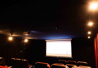 Donkere cinemazaal met lege rode stoelen, verlicht scherm en zachte verlichting op een glamping.
