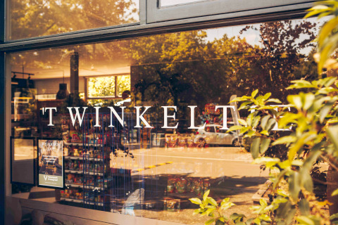 Entrée d’un hébergement glamping avec 'TWINKELT' sur la vitre et vue sur l’intérieur du magasin.