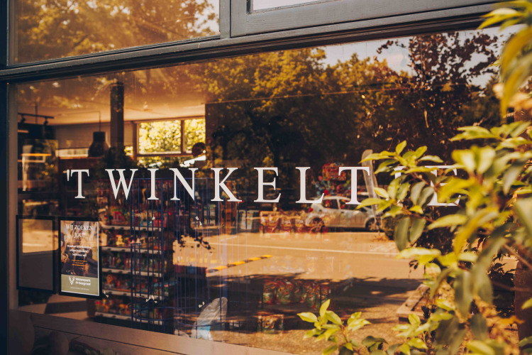 Entrada de un alojamiento glamping, ventana con 'TWINKELT' y vista al interior de la tienda y naturaleza.