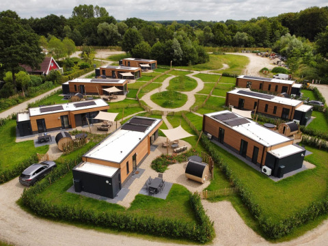 Luchtfoto van moderne lodges te midden van groen, met wandelpaden en geparkeerde auto's in een natuurgebied.