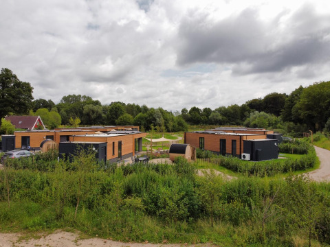Lodges modernes en bois entourés de verdure luxuriante sous un ciel nuageux, dans un cadre paisible.