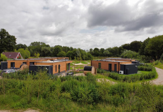 Moderne houten lodges omringd door weelderig groen in een rustige, landelijke omgeving onder wolken.