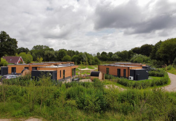 Lodges modernes en bois entourés de verdure luxuriante sous un ciel nuageux, dans un cadre paisible.