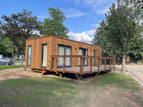 Een moderne houten lodge met groot terras, omgeven door bomen en groen op een natuurvriendelijke locatie.