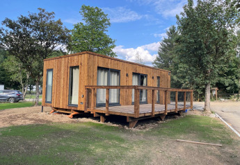 Et moderne træhus med stor terrasse i en naturskøn lodge, omgivet af træer og grønne områder.