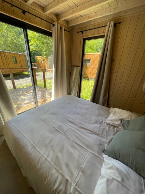 Slaapkamer in een houten Eco Lodge bij Hameau de l'Ourthe in België, met grote ramen en buitenzicht.