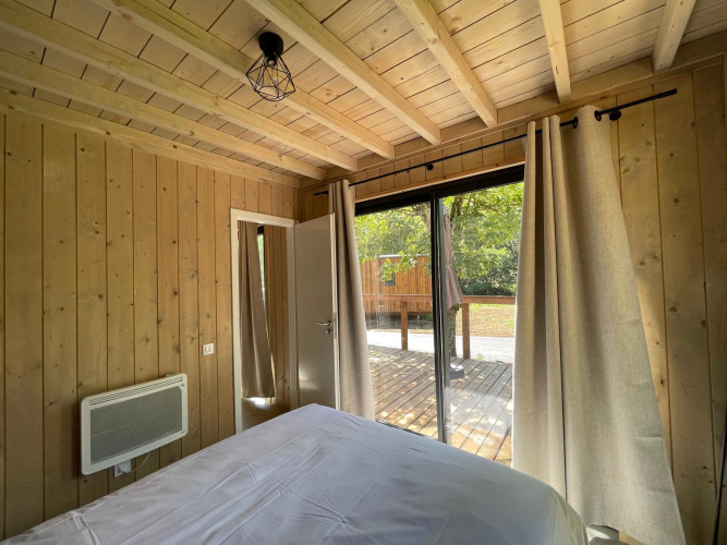 Dormitorio en Eco Lodge en Hameau de l'Ourthe, Bélgica, con paredes de madera y acceso a la terraza.