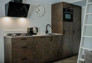 Moderne tiny house keuken met gaskookplaat, oven, waterkoker, klok en houtlook keukenkasten.