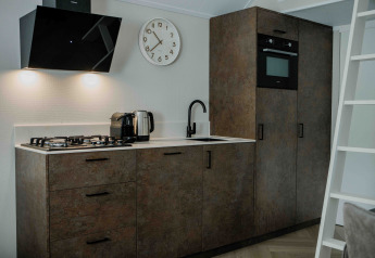 Modern tiny house kitchen with gas stove, oven, electric kettle, wall clock, and wood-look cabinets.