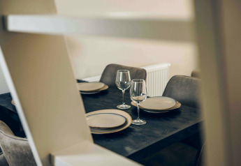 Mesa de comedor moderna con platos y copas de vino en Tiny Loft, Veluwepark de Bosgraaf, Países Bajos.