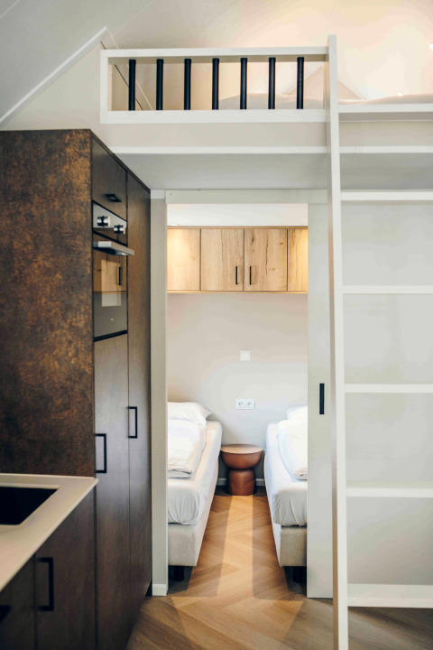 Modern tiny house interior showing kitchen, loft area, and two single beds with minimalist, clean design.