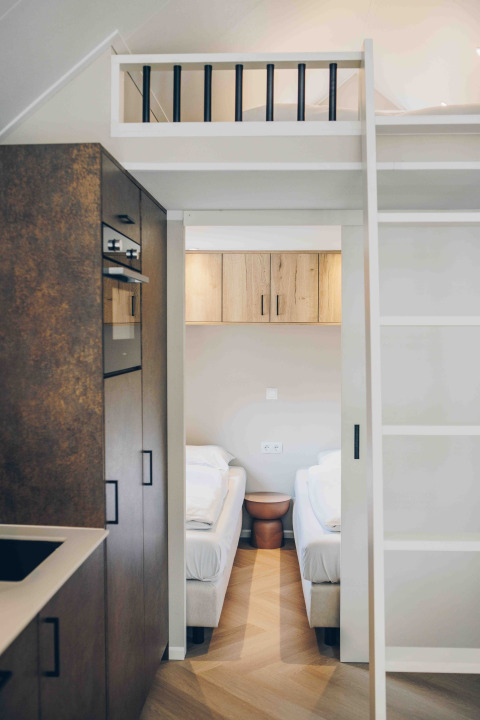 Interni di una tiny house moderna con cucina, soppalco e due letti singoli, stile chiaro e minimalista.