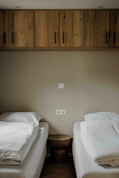 Due letti singoli con biancheria bianca, comodino marrone e armadietti in legno in una tiny house.