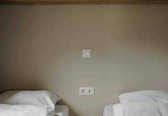 Two single beds with white bedding, a small brown nightstand and wooden cabinets in a tiny house room.