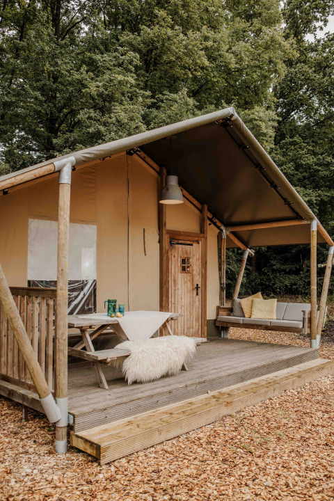 Safari-Zelt im Veluwepark de Bosgraaf in den Niederlanden mit Holzterrasse, Bank und Waldhintergrund.