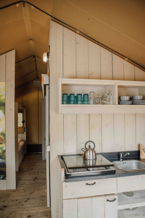 Interior de tienda safari en Veluwepark de Bosgraaf, Países Bajos, con cocina y estantes con vajilla.