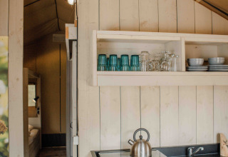 Interior de tienda safari en Veluwepark de Bosgraaf, Países Bajos, con cocina y estantes con vajilla.