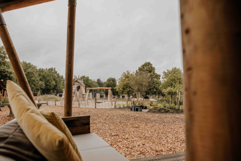 Udsigt fra en safaritelts veranda på Veluwepark de Bosgraaf, med legeplads og natur i Holland.