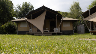 Front view of Safari House safari tent with shade canopy, surrounded by grass and trees on a sunny day.