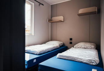 Et værelse med to enkeltsenge, blå madrasser, hvide dyner, hylder og et vindue hos Loggia Wood, Eurocamping Vessem BV.