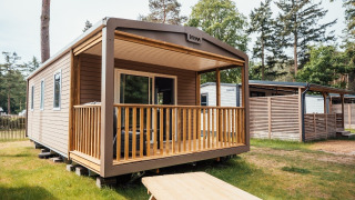 Loggia Wood lodge with a covered wooden porch and outdoor seating set in a tranquil forest environment.