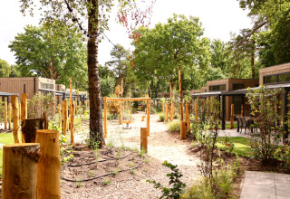 Moderne lodges met omliggende tuin, zandpaden, houten palen en veel groen in een rustige setting.
