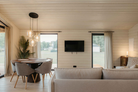 Moderne woonkamer in Panorama Lake House Scandi met ronde eettafel, grijze bank en grote ramen bij Wilsumer Berge.