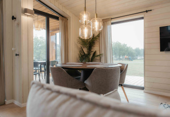 Essbereich im Panorama Lake House Scandi mit großen Fenstern, grauen Stühlen und stilvollen Lampen.