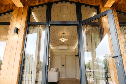 Open glazen deuren van Panorama Lake House Scandi met zicht op een modern houten interieur en plafond.