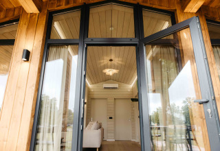 Open glazen deuren van Panorama Lake House Scandi met zicht op een modern houten interieur en plafond.