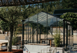 Zona de descanso al aire libre en un alojamiento glamping con sillas blancas modernas y un invernadero de vidrio.