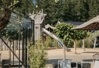 Spielplatz mit Rutsche und Glamping-Unterkunft, umgeben von Bäumen und entspannter Atmosphäre.