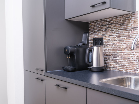 Cocina moderna en un lodge con hervidor eléctrico, cafetera, gabinetes grises y fregadero acero.