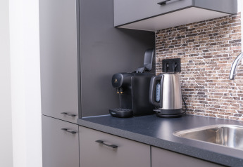 Modern kitchenette in a lodge with electric kettle, coffee machine, gray cabinets, and sink area.